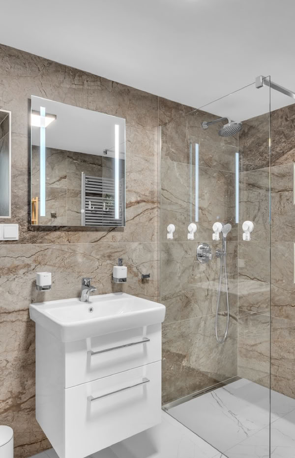 Modern bathroom with stone tile walls, a glass shower enclosure, a white vanity with a mirror above, and a wooden shelving unit.